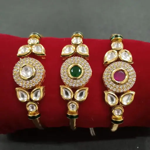 Set of three gold bangles with round kundan centerpieces in white, green, and pink stones on a red display roll – traditional Indian jewelry.