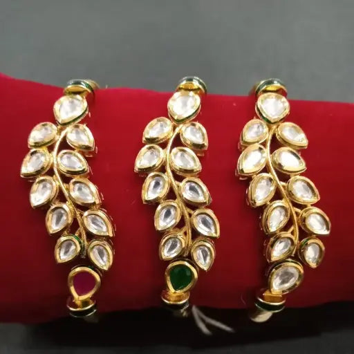 Elegant gold bangle set with leaf-shaped kundan stones and green/red accents, inspired by nature – displayed on red velvet