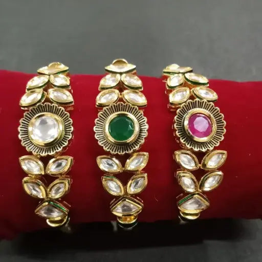 Bold gold bangle trio with large round kundan centerpieces in white, emerald green, and ruby pink – rich traditional design.