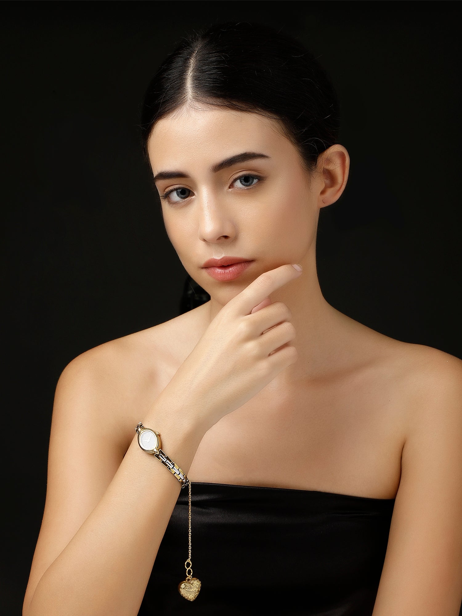 AIVY LUXE gold heart watch charm hanging from a silver bracelet worn by a woman in a black strapless top