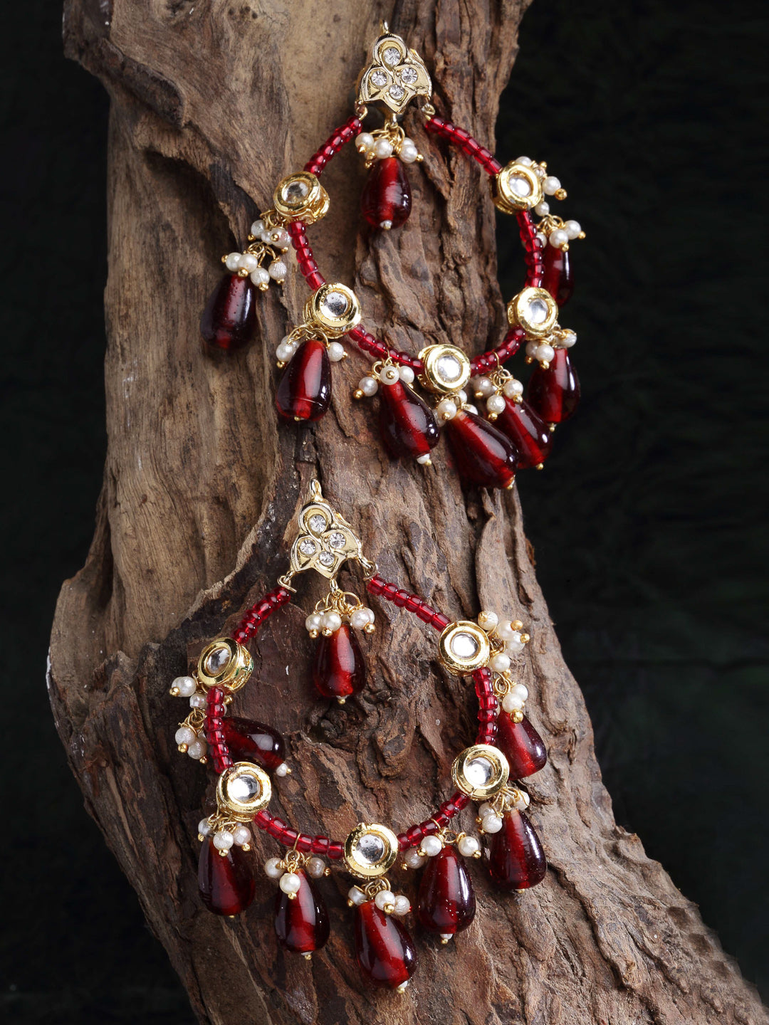 AIVY LUXE red stone statement earrings with gold land pearl accents hanging on rustic wood